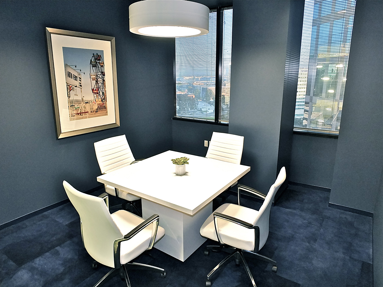 An Omnience pendant in an office lighting application above a small meeting table in a blue-carpeted meeting room.